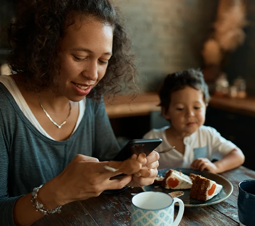 Mother sitting with her young son at a kitchen table while checking a smartphone, representing how Parent Link helps parents manage shared schedules and daily routines.