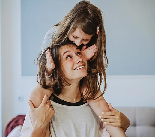 Mother smiling while carrying her daughter on her shoulders, representing how Parent Link helps parents manage shared expenses and stay coordinated.