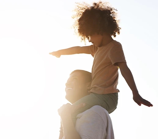 Father smiling while carrying his daughter on his shoulders outdoors in bright sunlight, representing how Parent Link helps families stay informed and connected with shared resources.