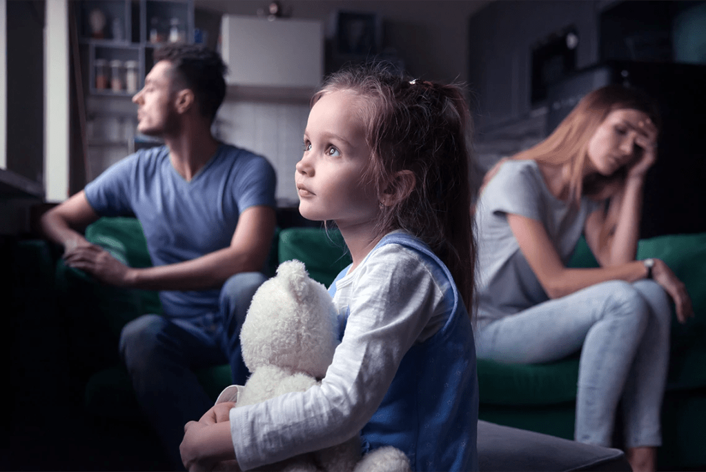 A young girl holding a teddy bear while sitting between her parents during a difficult conversation.